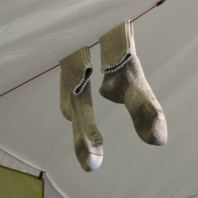 Ein Paar abgenutzte Socken, die an einer Leine auf einem Campingplatz im Freien in der Nähe des Robens® Voyager Versa 3-Zeltes hängen.