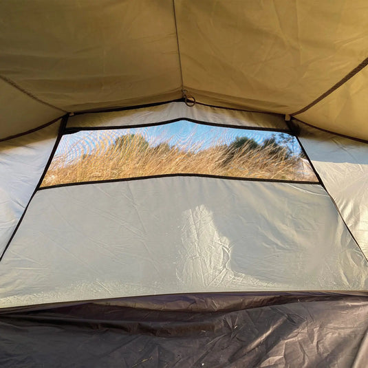 Blick auf Gras durch das Fenster eines Robens® 3-Personen Zelt Voyager Versa 3 mit einströmendem Sonnenlicht.