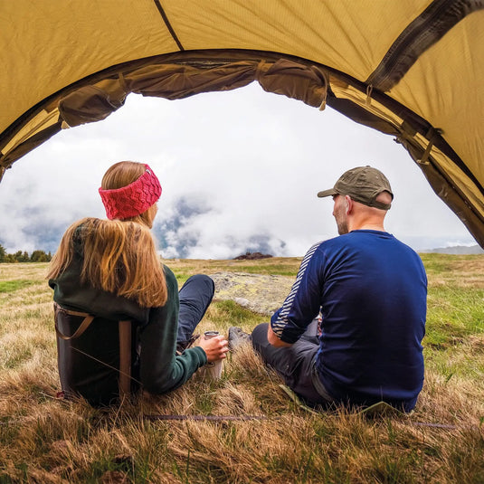 Zwei Personen sitzen am Eingang eines Robens® 4-Personen Zelt Voyager Versa 4 und genießen den Blick auf die Berge.