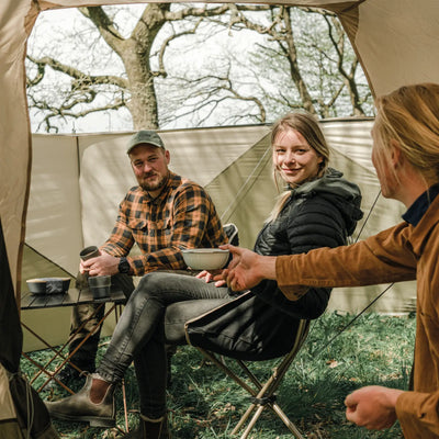 Eine Gruppe von Freunden genießt eine Mahlzeit auf einem Campingplatz in ihrem Robens® 4-Personen-Zelt – Double Dreamer 4.