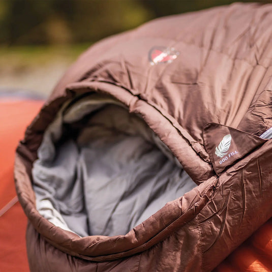 Nahaufnahme eines braunen Robens® Schlafsack Serac 600 -14°C mit der Aufschrift „Serac 600 Fill Power“, vorbereitet für Camping im Freien.