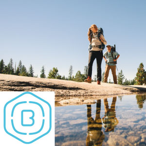 Zwei Personen wandern in der Natur und spiegeln sich in einer Wasserfläche.