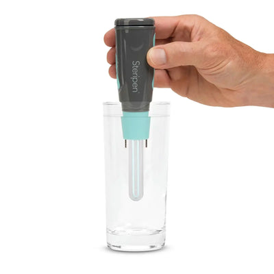 Hand hält einen Wasserreiniger Steripen® Aqua UV - Wasseraufbereitung, der in ein Glas Wasser eingesetzt wird.