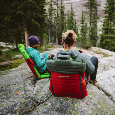 Zwei Wanderer genießen eine Pause auf Therm-a-Rest® Trekker Chairs inmitten der Natur.