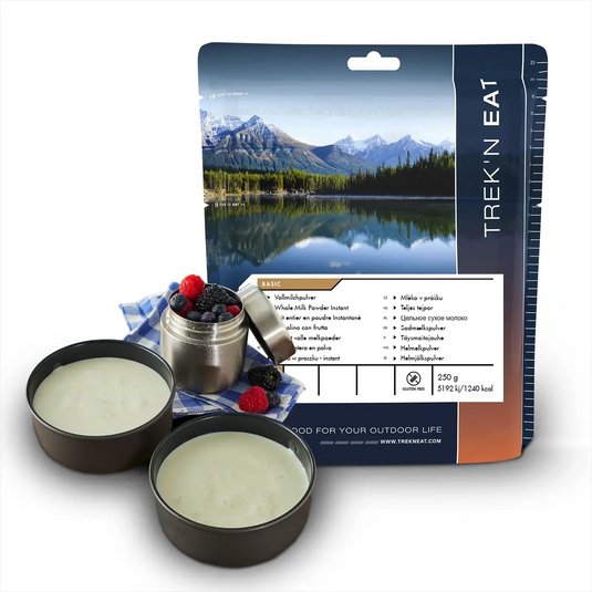 Verpackte Outdoor-Mahlzeit mit einem malerischen Bergsee auf der Verpackung, präsentiert neben zubereiteten Speisen in Campingschalen, darunter Trek'n Eat Vollmilchpulver.