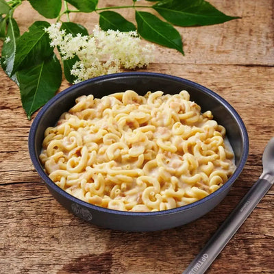 Eine Schüssel mit cremigem Trek'n Eat Mac'n Cheese, serviert auf einem Holztisch mit einem Löffel daneben.