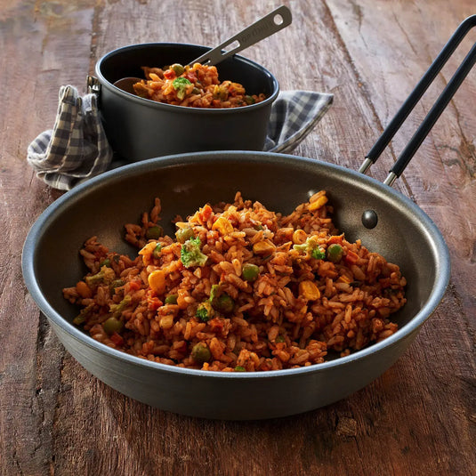 Ein Topf und eine Pfanne gefüllt mit Trek'n Eat Jambalaya gemischt mit Gemüse auf einer Holzoberfläche.