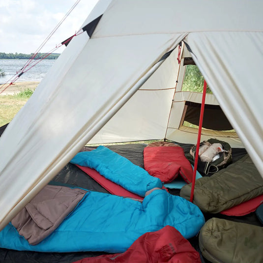 Ein Blick auf den Innenraum eines Campingzeltes mit ausgebreiteten Schlafsäcken des Typs Grand Canyon® Utah 205 - Schlafsack, aufgestellt am Seeufer.