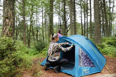 Zwei Personen bauen in einem Wald ein blaues Vango™ „Alpha 400“ Kuppelzelt auf.