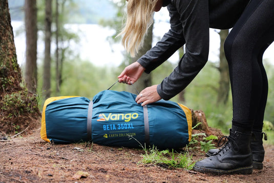 Eine Person in Outdoor-Kleidung packt in einem Waldgebiet ein Vango™ „Beta 350XL CLR“ Tunnelzelt für 3 Personen ein oder aus.