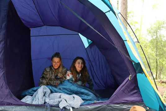 Zwei Menschen lächeln in einem Vango™ „Beta 550XL CLR“ Tunnelzelt in einer Waldumgebung.