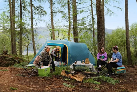 Drei Personen entspannen sich auf einem Campingplatz im Wald, in der Nähe steht ihr Vango™ „Beta 550XL CLR“ Tunnelzelt.