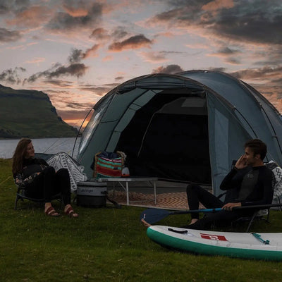 Zwei Personen entspannen sich an einem Zelt mit Campingausrüstung, darunter ein Vango™ „Cragmor 500“ Kuppelzelt, 5-Personen, mit Blick auf eine malerische Landschaft in der Abenddämmerung.