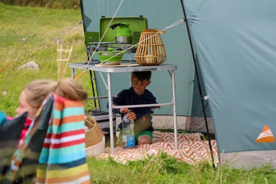 Ein Kind spielt in einem Vango™ „Harris 350“ Tunnelzelt auf einem Campingplatz, der mit Outdoor-Kochgeräten ausgestattet ist.