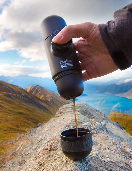 Kaffee wird aus Thermoskanne in Becher in Berglandschaft gegossen.